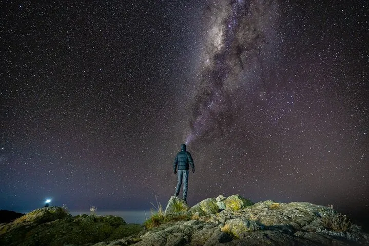 Climber standing under the Milky Way on a rocky ridge on a Kilimanjaro climbing tour by the Lemosho Route, Tanzania
