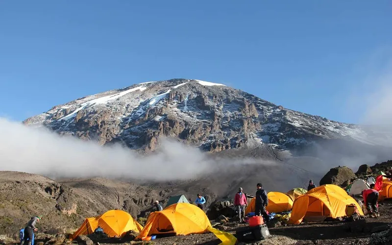 Orange tents at a high camp below the snowy Kibo crater on a Kilimanjaro climbing tour by the Umbwe Route, Tanzania