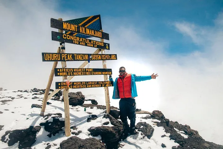 Climber in a red jacket at the Uhuru Peak sign on a Kilimanjaro climbing tour by the Machame Route, Tanzania