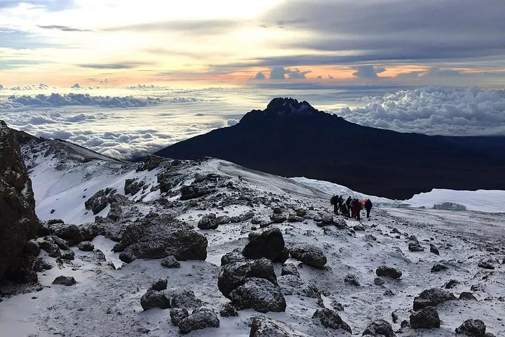 Snowy rocks and a line of trekkers above the clouds with Mawenzi behind on a Kilimanjaro climbing tour by the Rongai Route, Tanzania