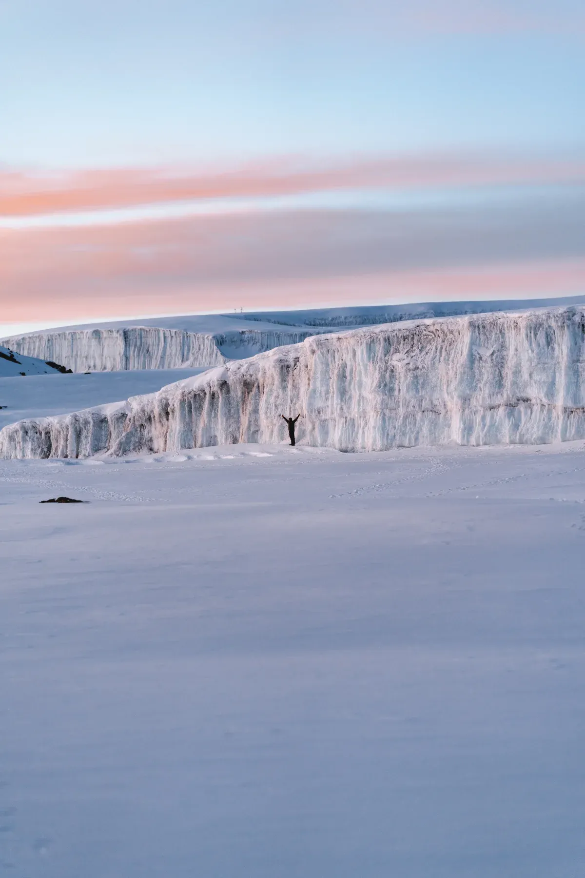 A climber dwarfed by the ice wall of the Furtwangler Glacier in the Kibo crater, a sight on Kilimanjaro climbing tours