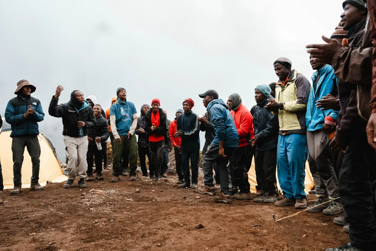 Porters singing and clapping in a circle at a high camp, the crew that every Kilimanjaro climbing tour tips at the end